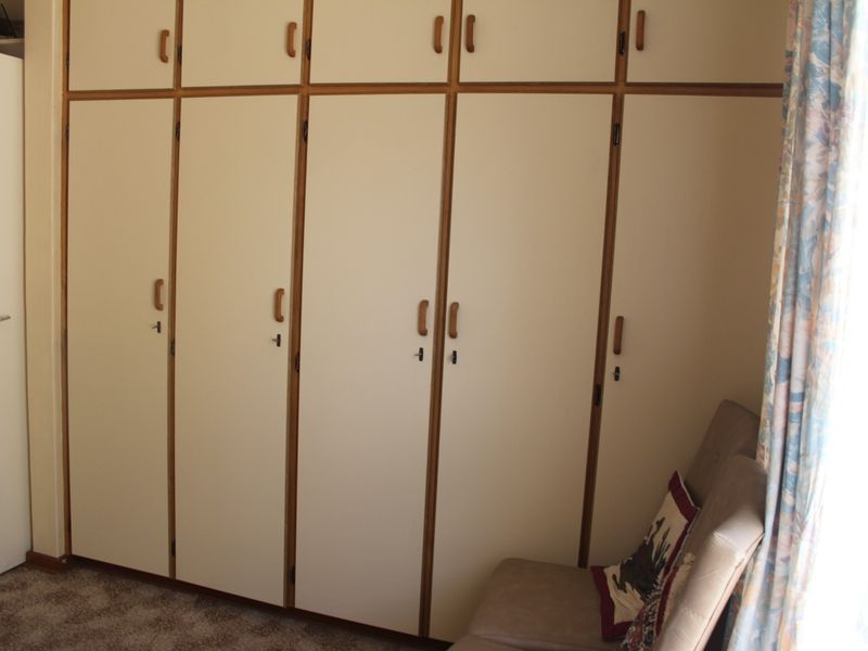 A bedroom featuring extensive floor-to-ceiling built-in cupboards with a dated finish and carpeted flooring.