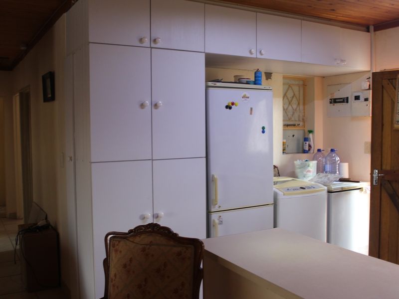 A functional kitchen area featuring built-in white cabinetry, a timber ceiling, and a security gate, offering a practical layout for daily use.