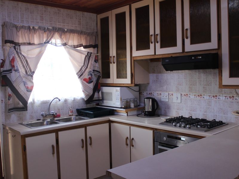 A functional kitchen featuring built-in cabinetry, a gas hob with extractor fan, stainless steel sink, and tiled backsplash with a timber ceiling finish.