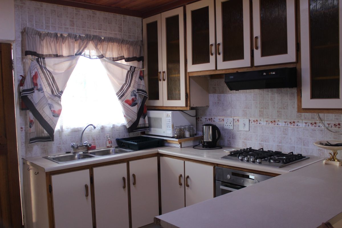 A functional kitchen featuring built-in cabinetry, a gas hob with extractor fan, stainless steel sink, and tiled backsplash with a timber ceiling finish.