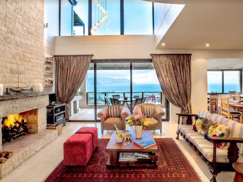 Spacious open-plan living area featuring a striking stone fireplace, double-volume ceilings, and expansive sliding doors opening to a scenic coastal view.