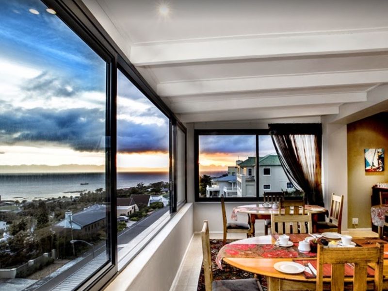 Bright dining area featuring expansive panoramic windows with stunning coastal and neighbourhood views, complemented by an exposed beam ceiling and recessed lighting.