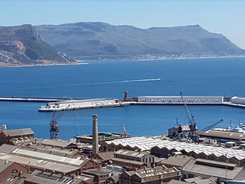 An elevated view overlooking a commercial harbour, industrial buildings, and the surrounding coastline with mountain scenery in the background.
