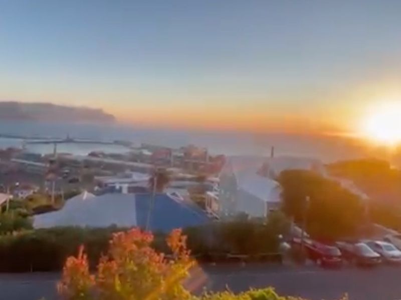 A scenic elevated view overlooking a coastal town and harbor at sunset.