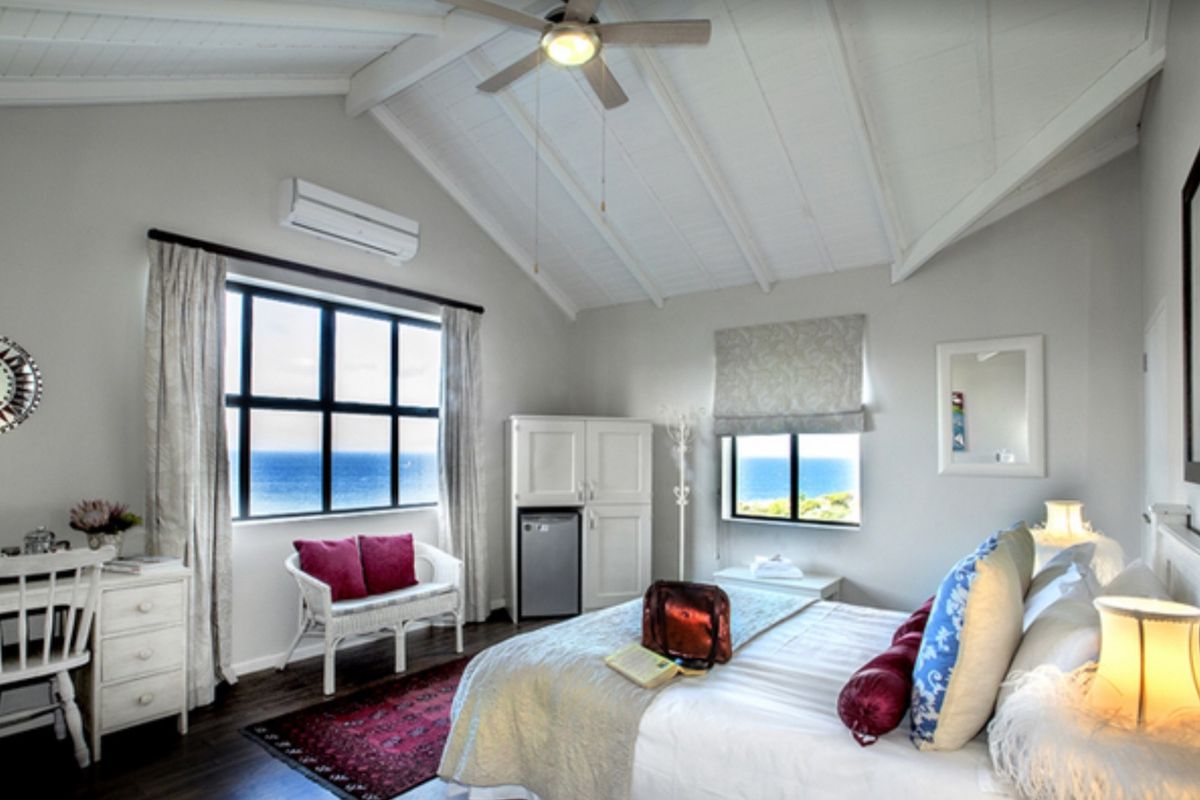 A bright bedroom featuring a vaulted ceiling, ceiling fan, split-system air conditioning, and large windows offering scenic ocean views.