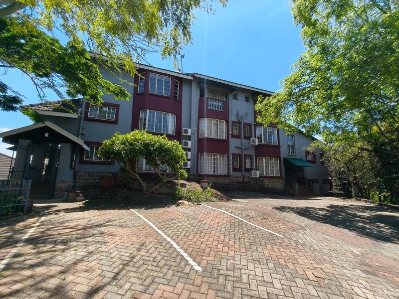 Front view of a multi-story residential building featuring a paved driveway, stone base detailing, and multiple window units with security bars.