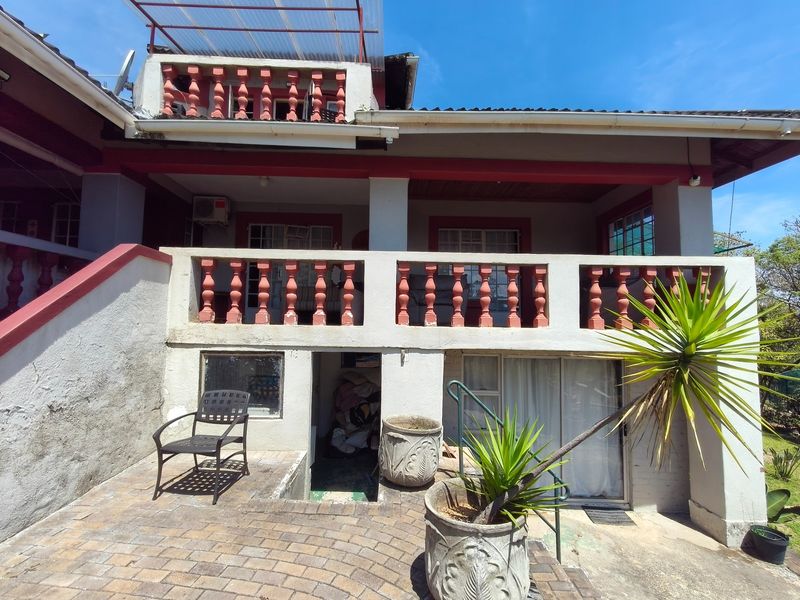 Rear exterior view of the house featuring a paved patio, covered veranda with balustrades, and sliding door access to the lower level.