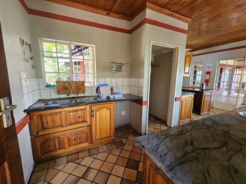 A functional kitchen featuring wooden cabinetry, granite countertops, a double basin sink, and a distinctive wooden ceiling with tiled flooring.