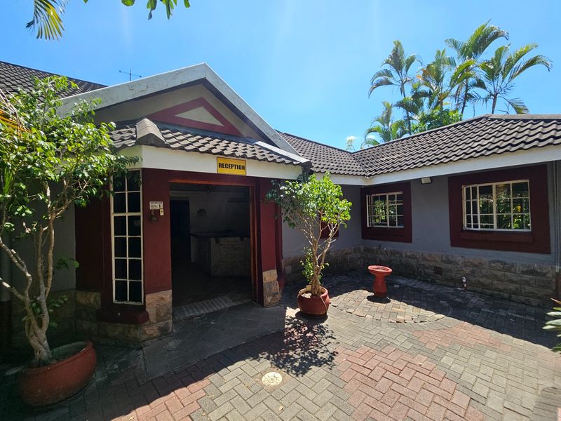 Front entrance area featuring a paved courtyard, stone cladding, and a reception doorway with a tiled roof structure.