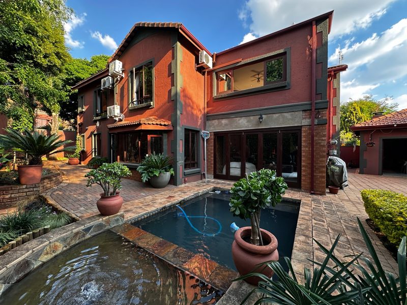 Rear exterior view featuring a paved patio area, a swimming pool with an integrated water feature, and a multi-story brick residence.