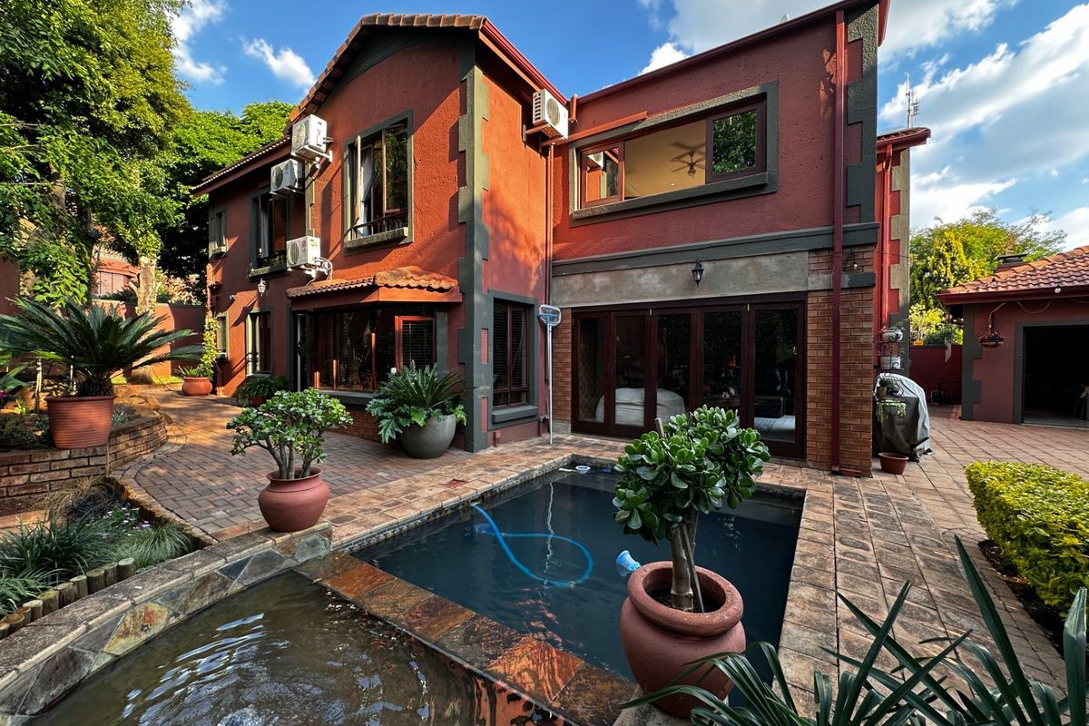 Rear exterior view featuring a paved patio area, a swimming pool with an integrated water feature, and a multi-story brick residence.