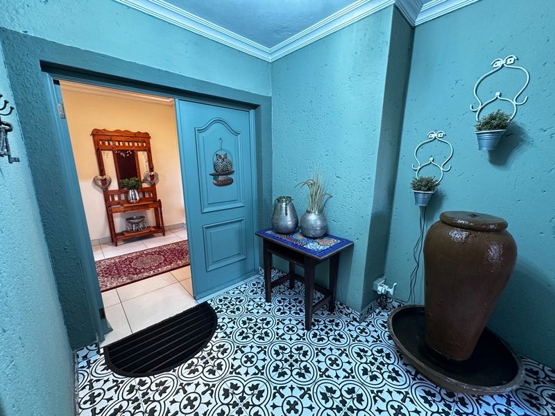 An inviting entrance hall featuring decorative patterned floor tiles, textured teal walls, and a coved ceiling, leading into an adjacent interior space.