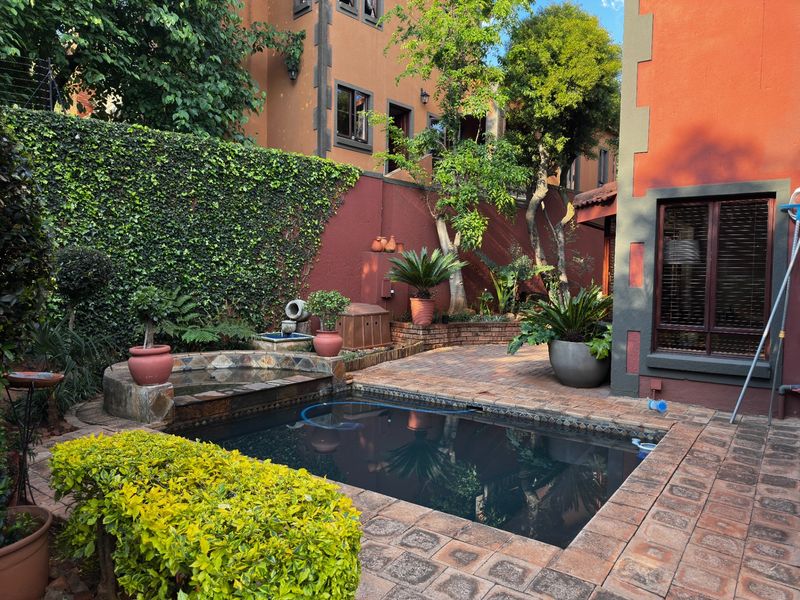 A private outdoor pool area featuring brick paving, a small water feature, and established garden landscaping against a terracotta-toned building facade.