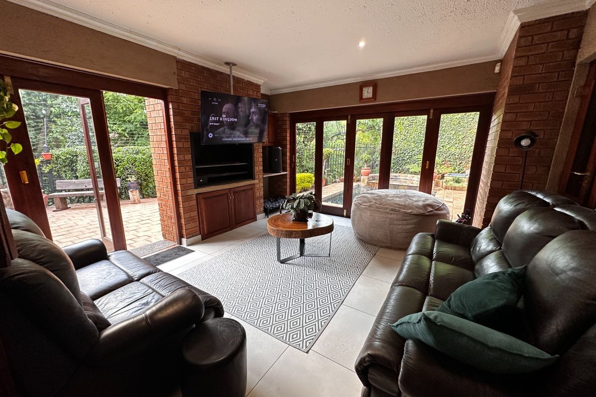 Spacious living room featuring exposed brick walls, tiled flooring, and large wooden folding doors that provide seamless access to the outdoor patio area.