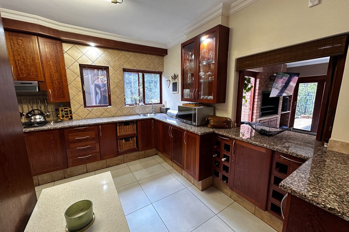 A well-maintained kitchen featuring rich wooden cabinetry, granite countertops, a built-in wine rack, and a tiled backsplash, with a convenient pass-through to the outdoor area.