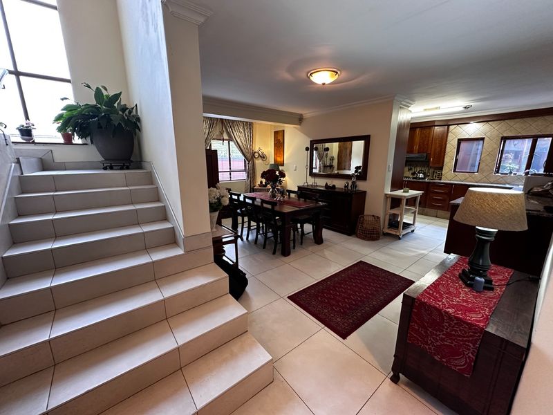 Spacious open-plan living and dining area featuring tiled flooring, a modern staircase, and a well-appointed kitchen with built-in cabinetry.