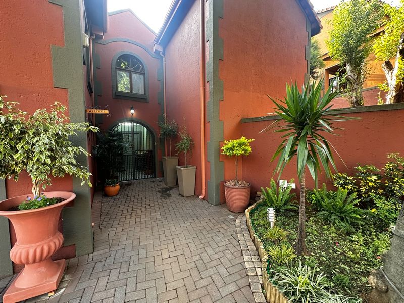 A charming entrance courtyard featuring brick paving, arched architectural details, and a secure metal gate leading to the main residence.