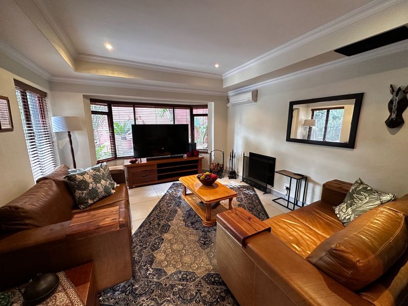 A comfortable living room featuring a bay window, tiled flooring, a fireplace, and a recessed ceiling with integrated lighting.