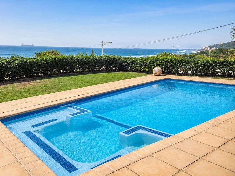 A well-maintained swimming pool area featuring a tiled surround and a landscaped hedge, offering scenic ocean views.