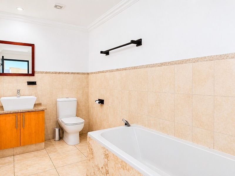 A clean, well-maintained bathroom featuring a vessel sink vanity, a standard toilet, and a tiled bathtub surround with neutral wall and floor tiling.