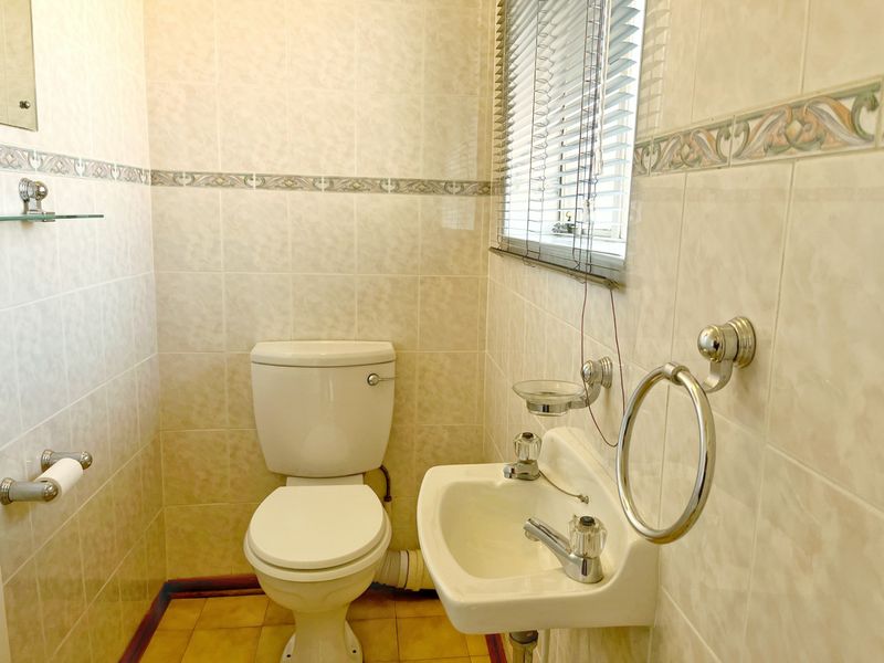 A compact guest bathroom featuring a wall-mounted basin and toilet with dated ceramic wall and floor tiling.