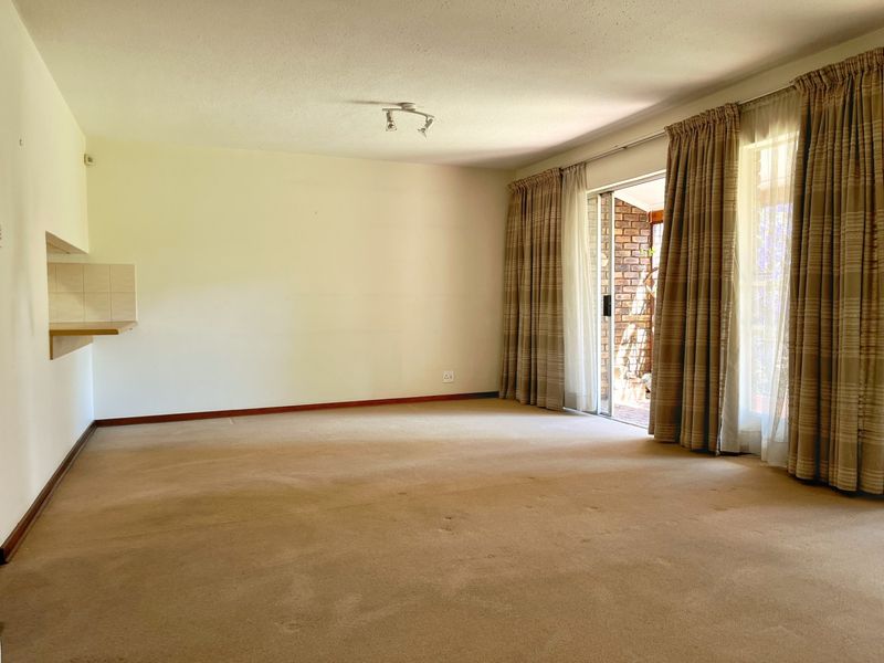 Spacious, empty living room featuring carpet flooring, a pass-through window to the kitchen, and a sliding glass door leading to an outdoor area.