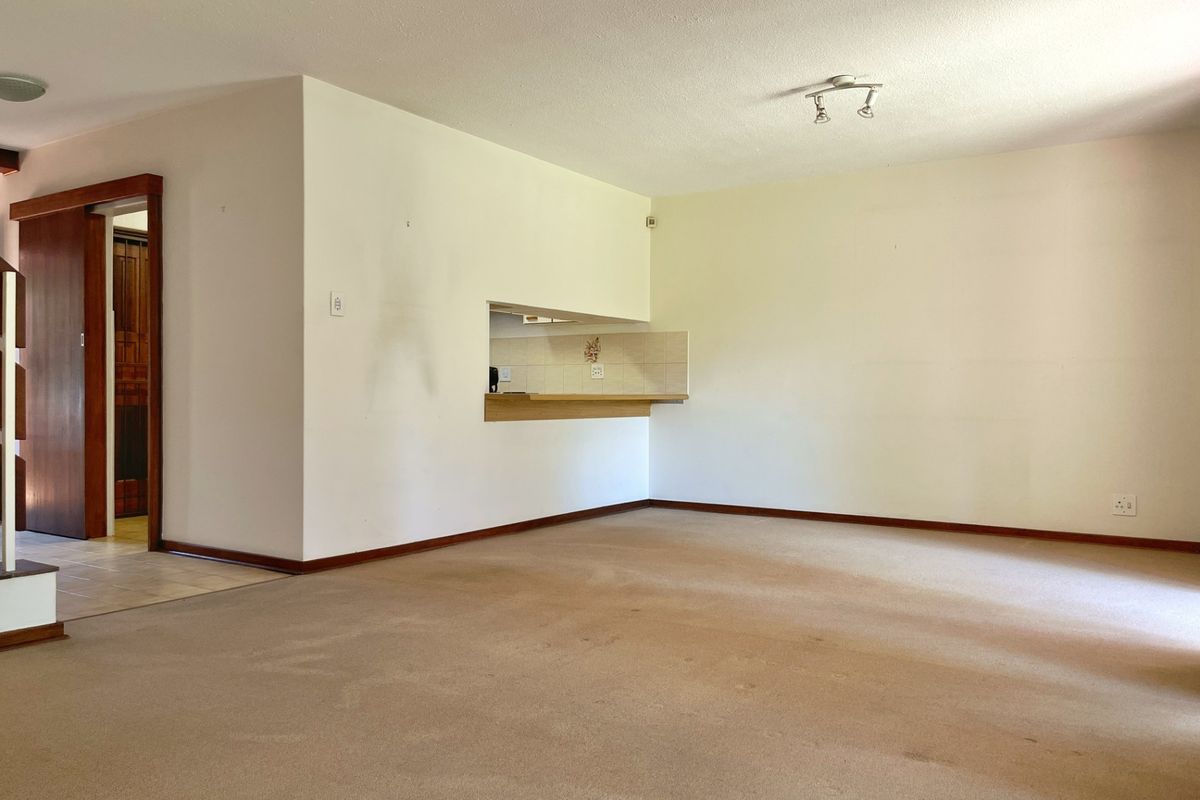 An empty living room featuring carpet flooring, a pass-through window to the kitchen area, and a sliding door leading to an adjacent space.