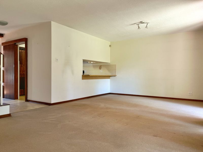 An empty living room featuring carpet flooring, a pass-through window to the kitchen area, and a sliding door leading to an adjacent space.