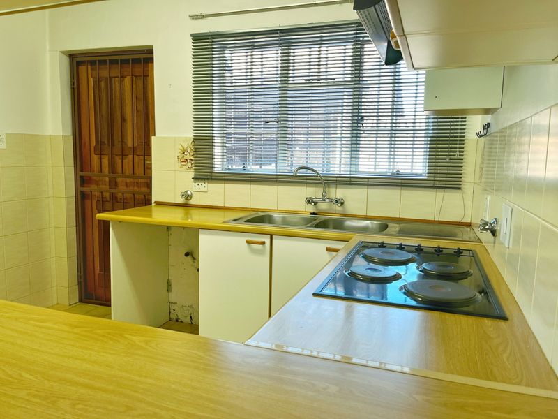 Functional kitchen featuring laminate countertops, electric hob, extractor fan, and double sink, with some cabinetry requiring repair or replacement.