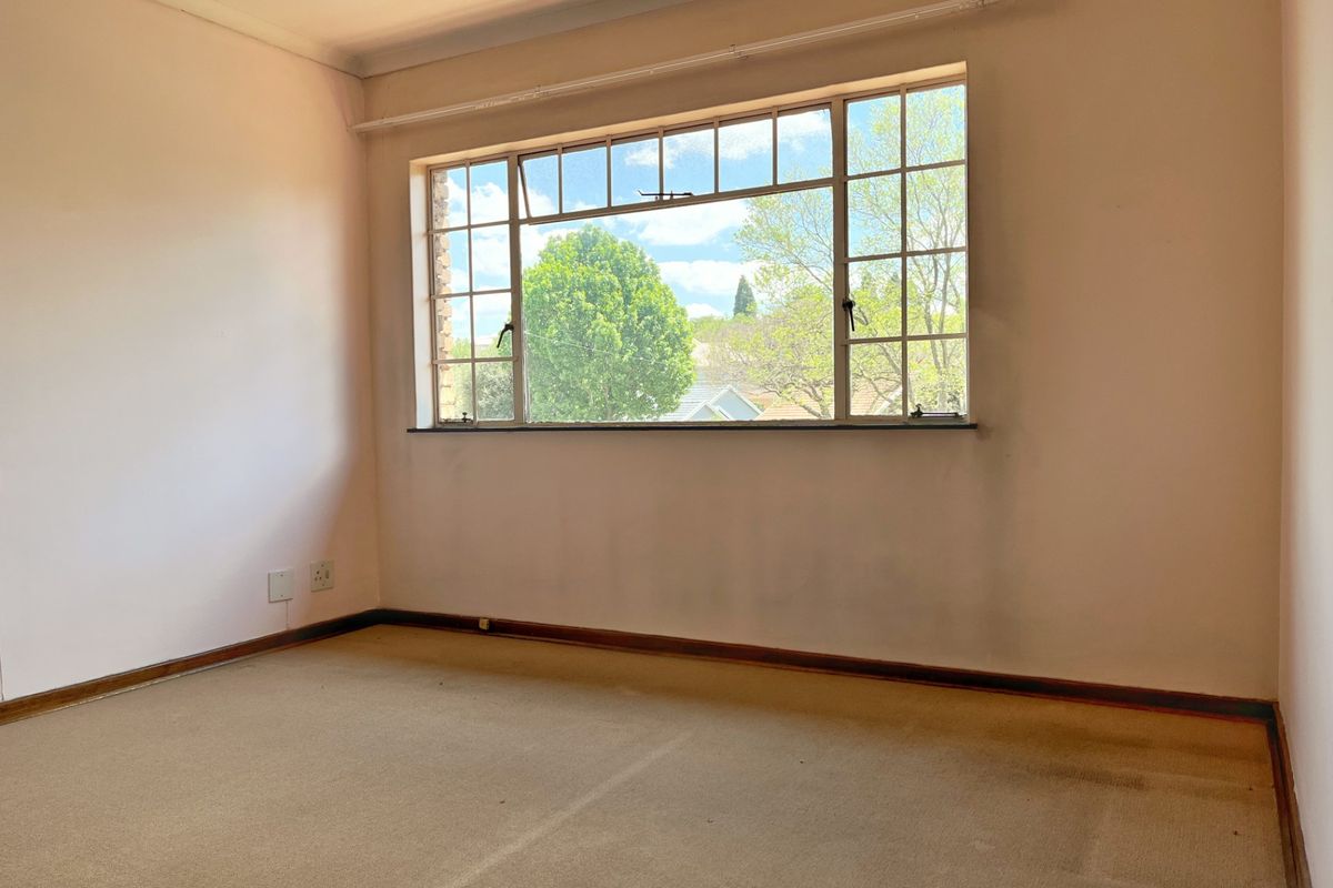 An empty bedroom featuring a large multi-pane window, carpeted flooring, and neutral wall finishes, offering a blank canvas for potential updates.
