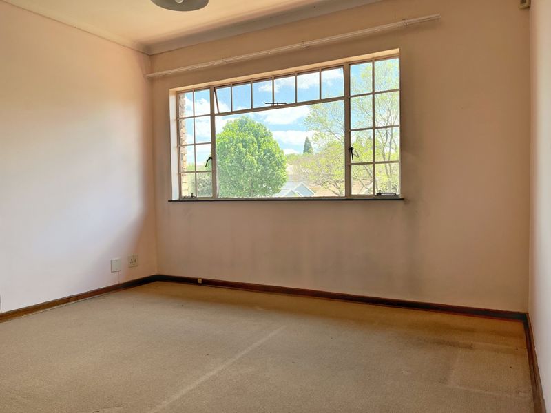 An empty bedroom featuring a large multi-pane window, carpeted flooring, and neutral wall finishes, offering a blank canvas for potential updates.