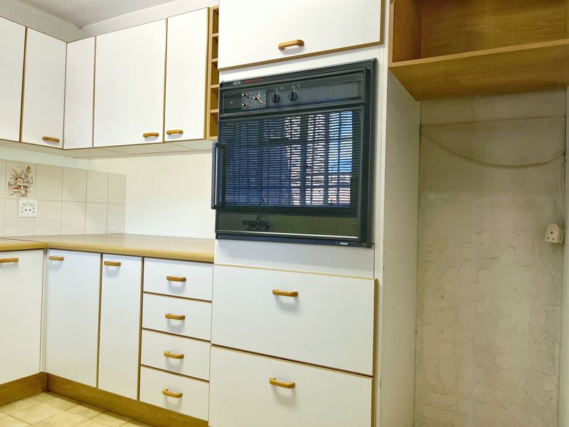 A dated kitchen featuring white cabinetry, laminate countertops, and a built-in oven, offering a blank canvas for modern renovation and design updates.