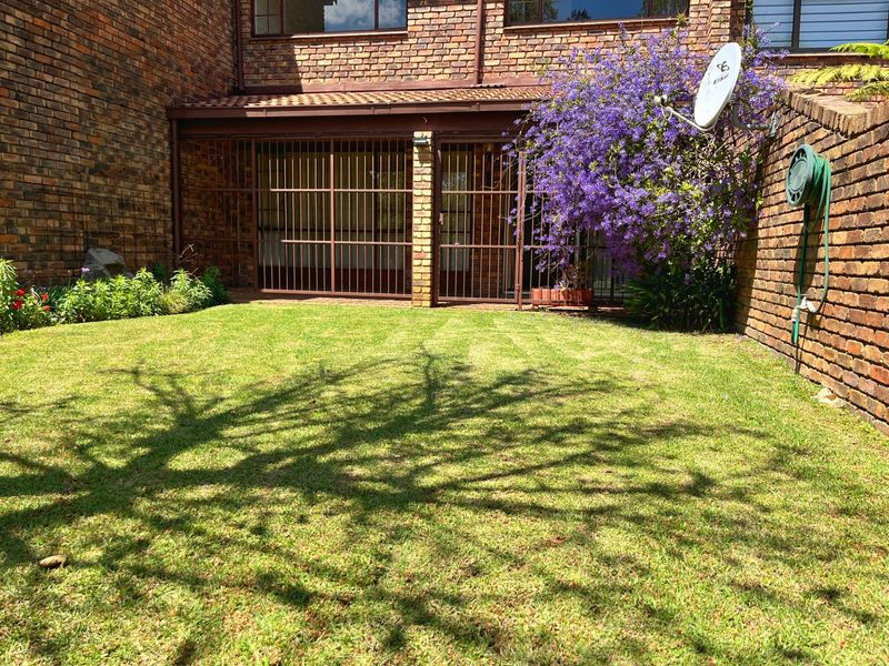 A private rear garden featuring a well-maintained lawn, brick townhouse facade, and a covered patio area secured with metal gates.