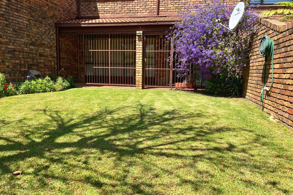 A private rear garden featuring a well-maintained lawn, brick townhouse facade, and a covered patio area secured with metal gates.