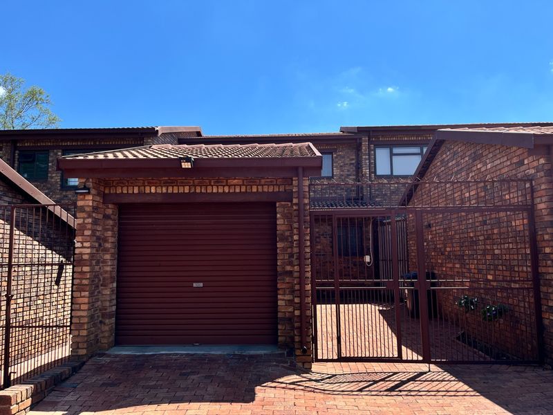 Front elevation of a townhouse featuring a face brick facade, tiled roof, secure roller shutter garage door, and a private gated entrance.