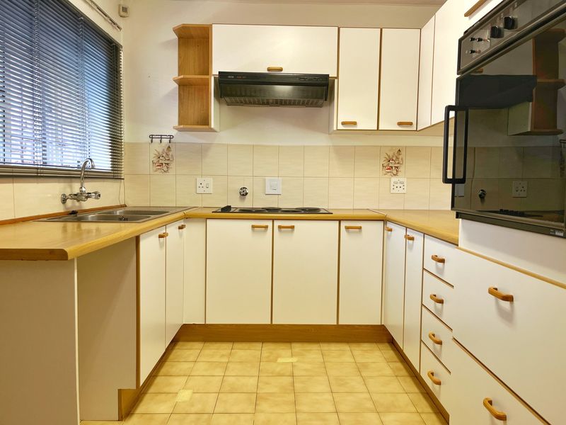 A functional U-shaped kitchen featuring white cabinetry, laminate countertops, built-in oven, electric hob, and tiled backsplash with neutral ceramic flooring.