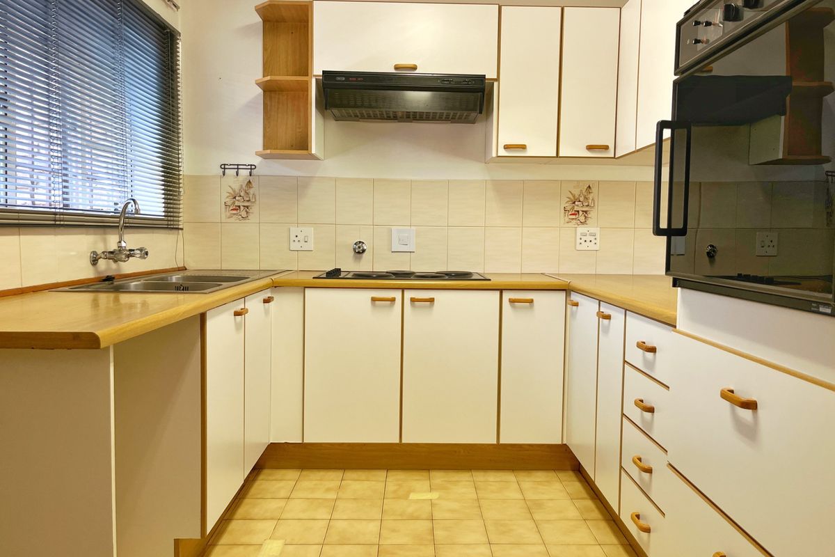 A functional U-shaped kitchen featuring white cabinetry, laminate countertops, built-in oven, electric hob, and tiled backsplash with neutral ceramic flooring.