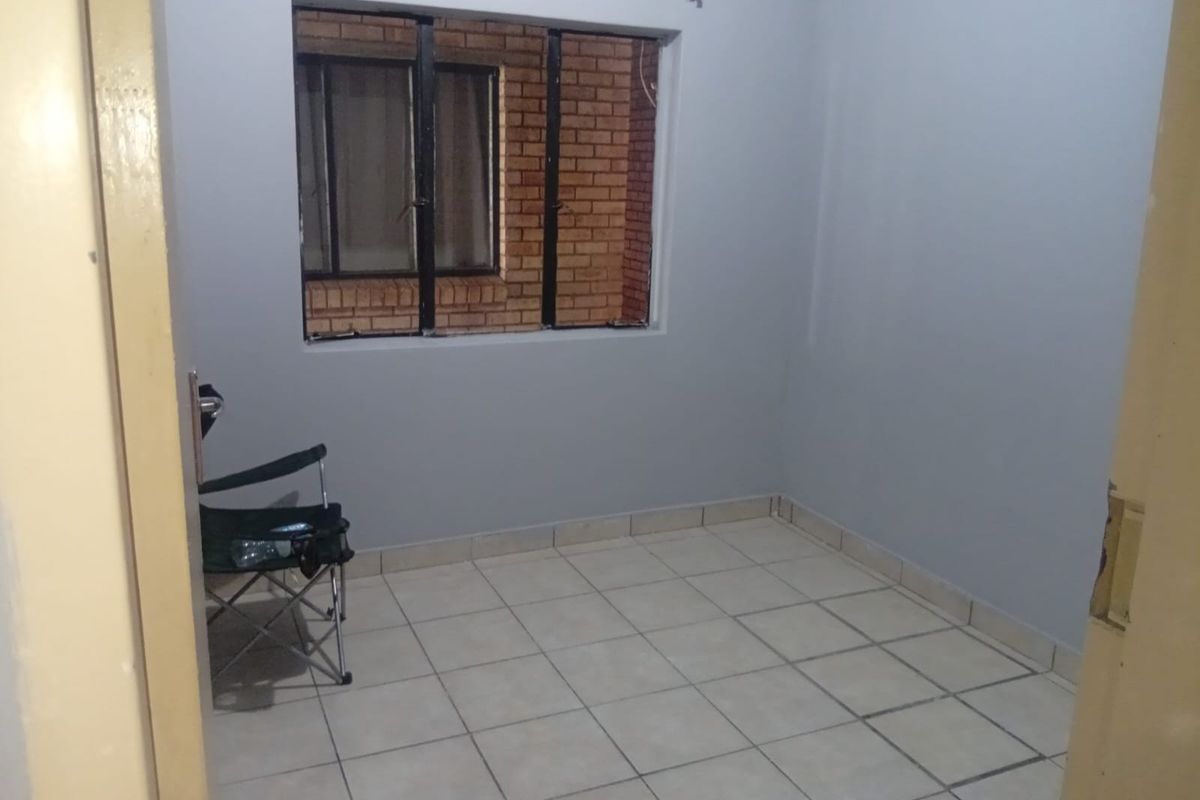 A compact, empty bedroom featuring tiled flooring and a metal-framed window, offering a blank canvas for personalization.