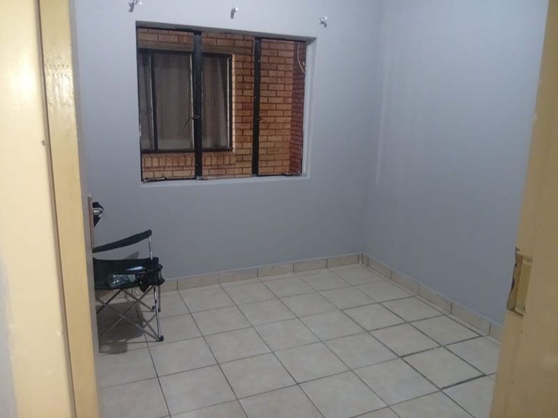 A compact, empty bedroom featuring tiled flooring and a metal-framed window, offering a blank canvas for personalization.