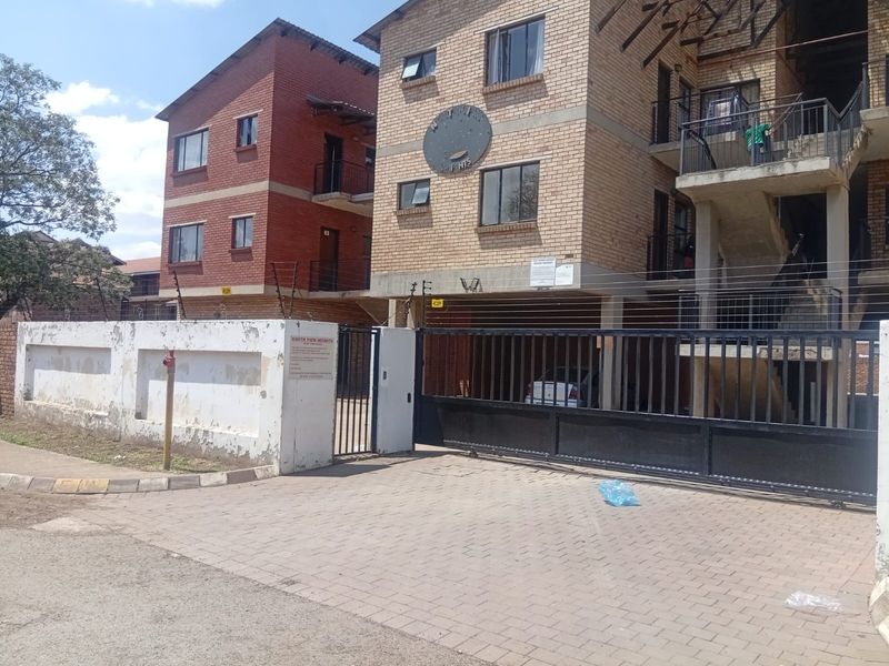 Front exterior view of a multi-story apartment complex featuring brick facade, secure gated entrance, electric fencing, and paved driveway access.