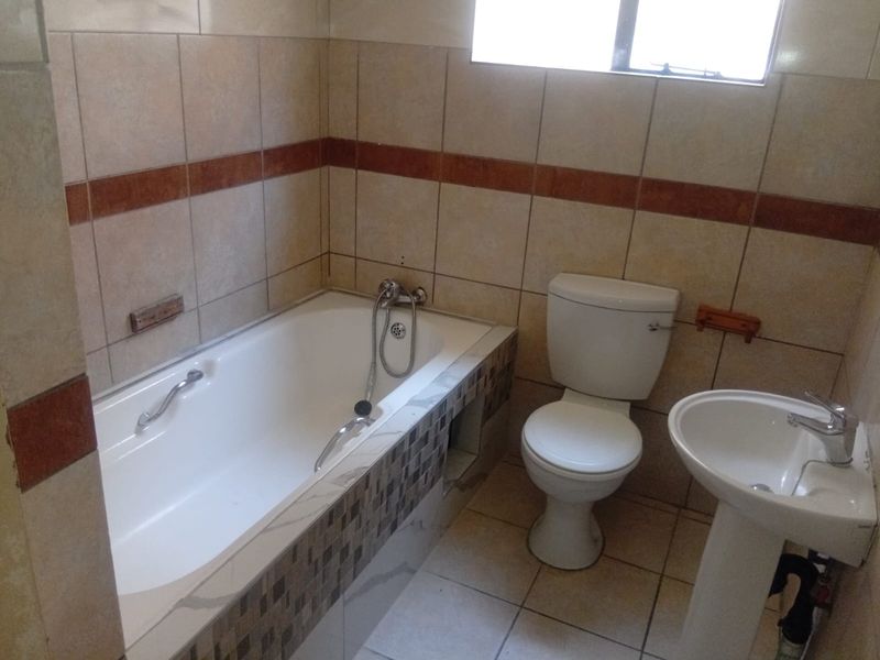 A functional bathroom featuring a built-in bathtub, pedestal basin, and toilet with neutral wall and floor tiling.