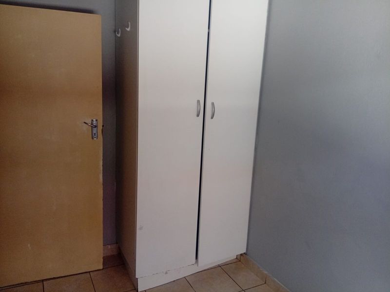 A bedroom interior featuring a built-in white wardrobe and tiled flooring, requiring minor cosmetic updates to the walls and door.