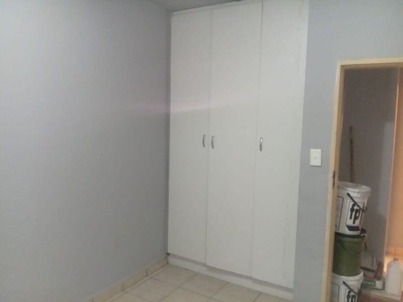 A simple bedroom featuring built-in cupboards and tiled flooring, offering a clean and neutral space ready for personalization.