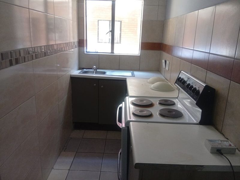 A compact kitchen featuring tiled walls, built-in cabinetry, a stainless steel sink, and a freestanding electric stove.