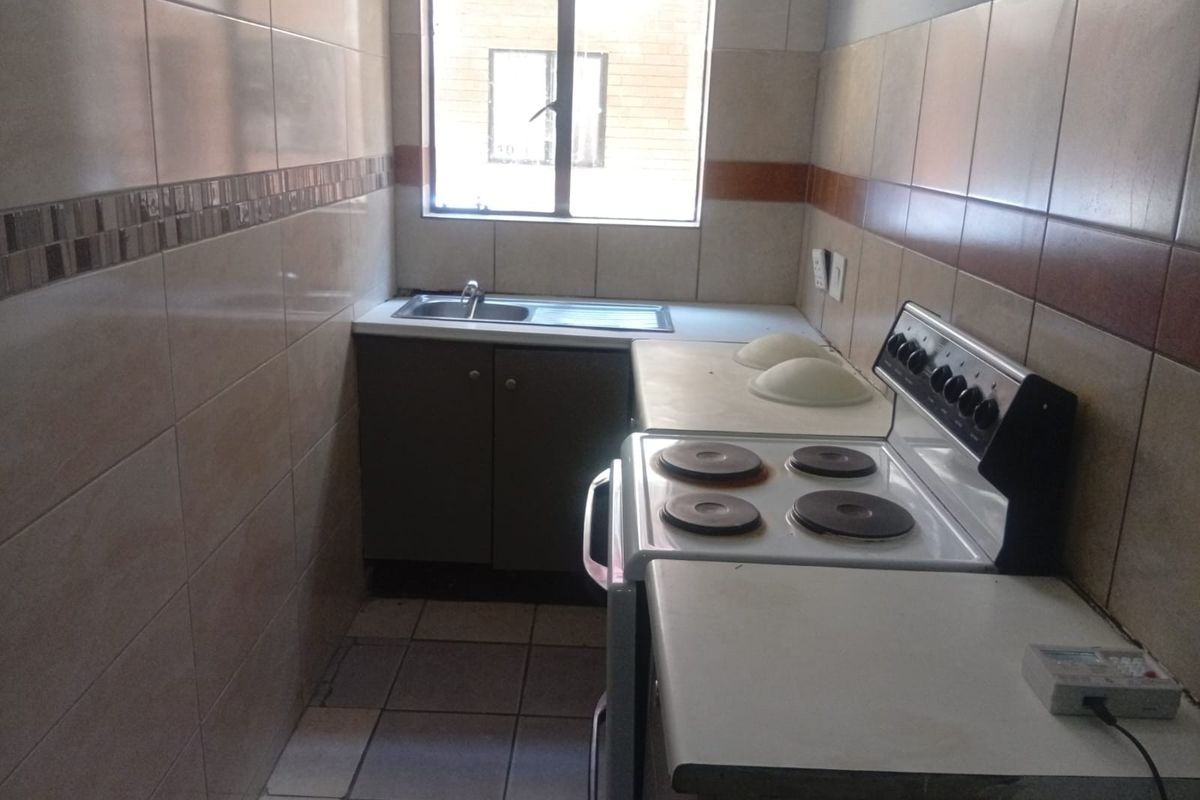 A compact kitchen featuring tiled walls, built-in cabinetry, a stainless steel sink, and a freestanding electric stove.