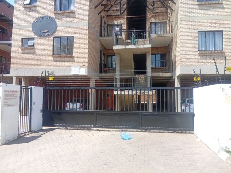 Front elevation of a face brick apartment complex featuring a secure sliding gate, electric fencing, and paved driveway access.