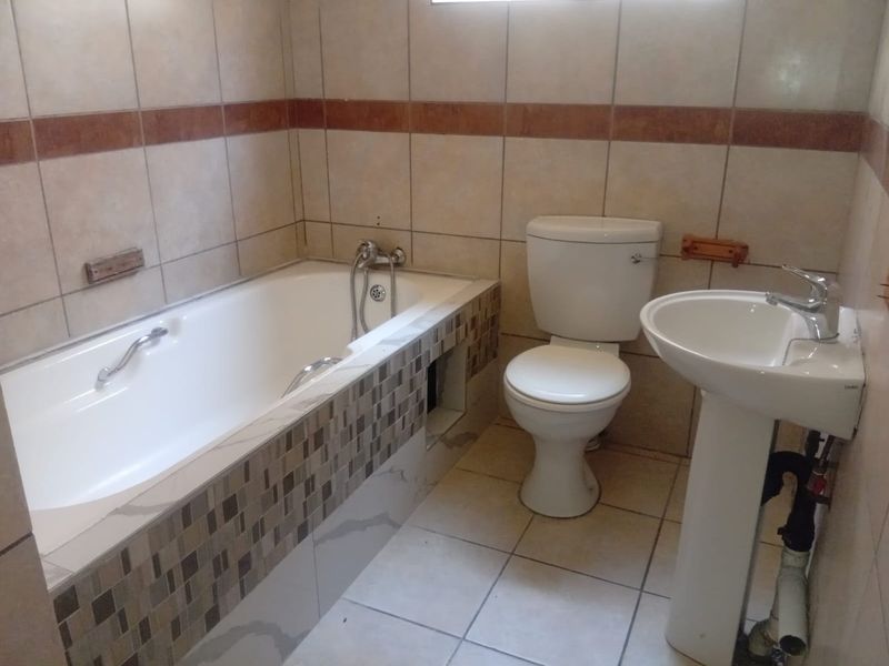 A functional bathroom featuring a bathtub, pedestal basin, and toilet with neutral wall and floor tiling.