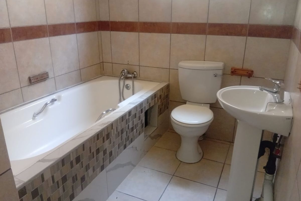 A functional bathroom featuring a bathtub, pedestal basin, and toilet with neutral wall and floor tiling.