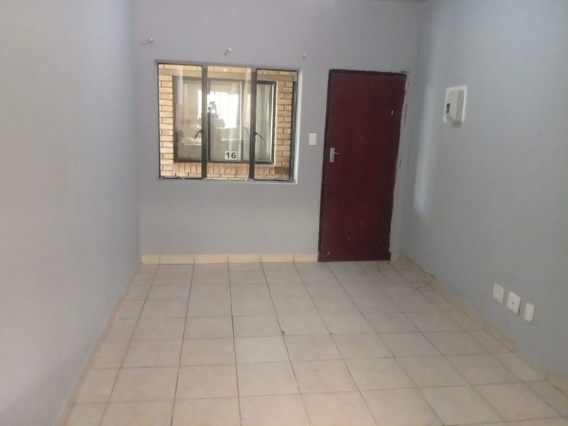 An empty living room featuring tiled flooring, a timber door, and an aluminium window, providing a blank canvas for interior design.