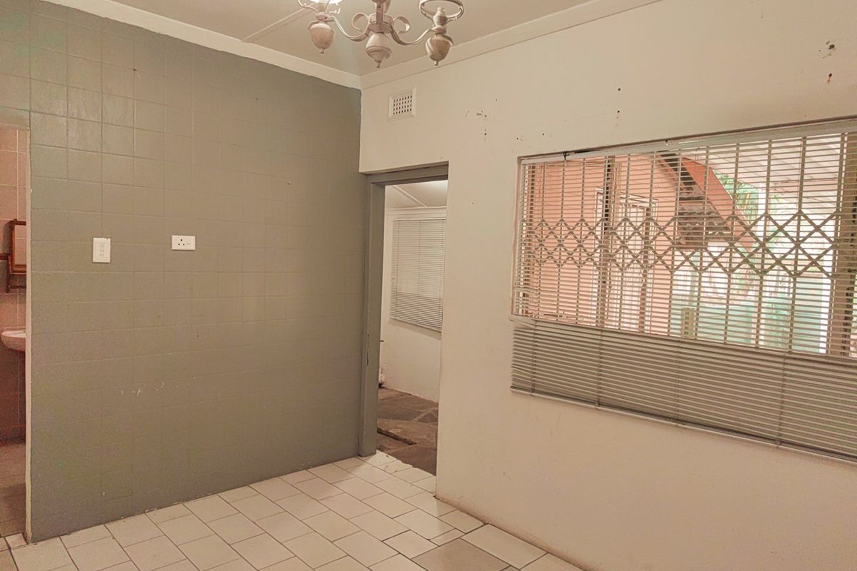 An empty living area featuring tiled flooring, a security gate on the window, and a central ceiling light fixture.